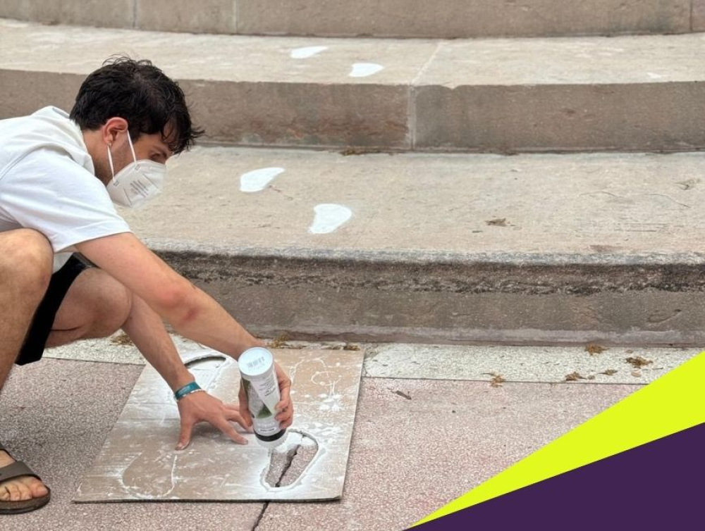 Eine Person sprüht mit einer Schablone und weißer Farbe Fußspuren an den Treppen eines Denkmals.