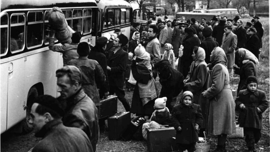 Schwarz-weiß-Fotografie einer Menschenmenge, die an einem Bus mit Gepäck und Kindern ansteht